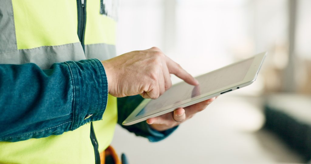 Construction worker holding tablet with digital blueprints on an industrial site